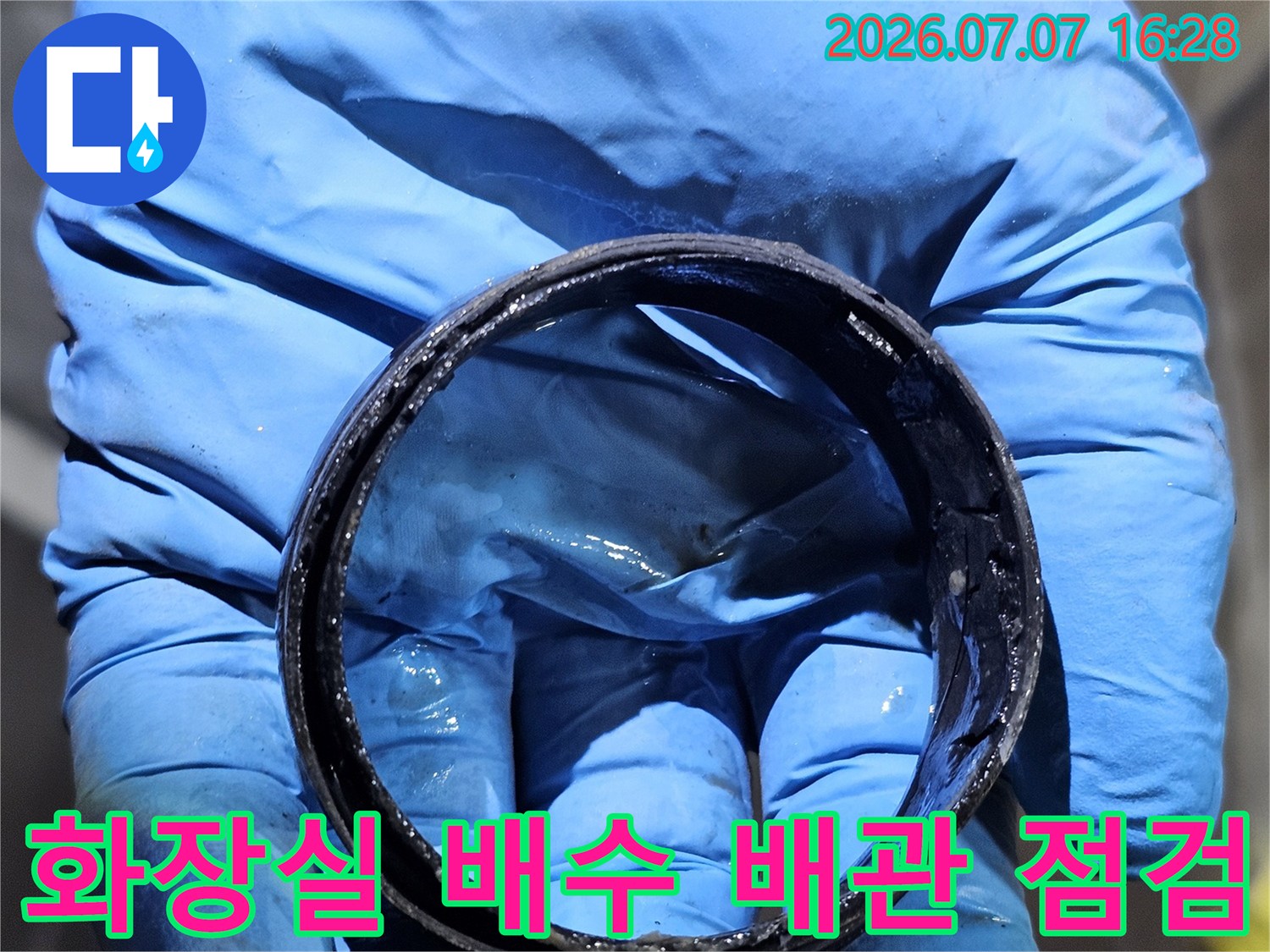 파란색 장갑을 낀 손으로 화장실 천장 내 노후된 배수 배관 연결 부위를 점검하는 모습