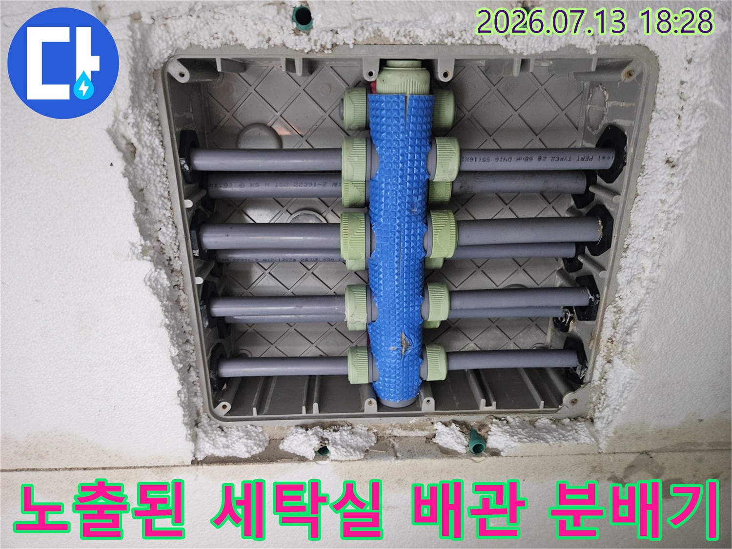 세탁실 바닥에 노출된 회색 배관과 파란색 밸브가 설치된 분배기 모습