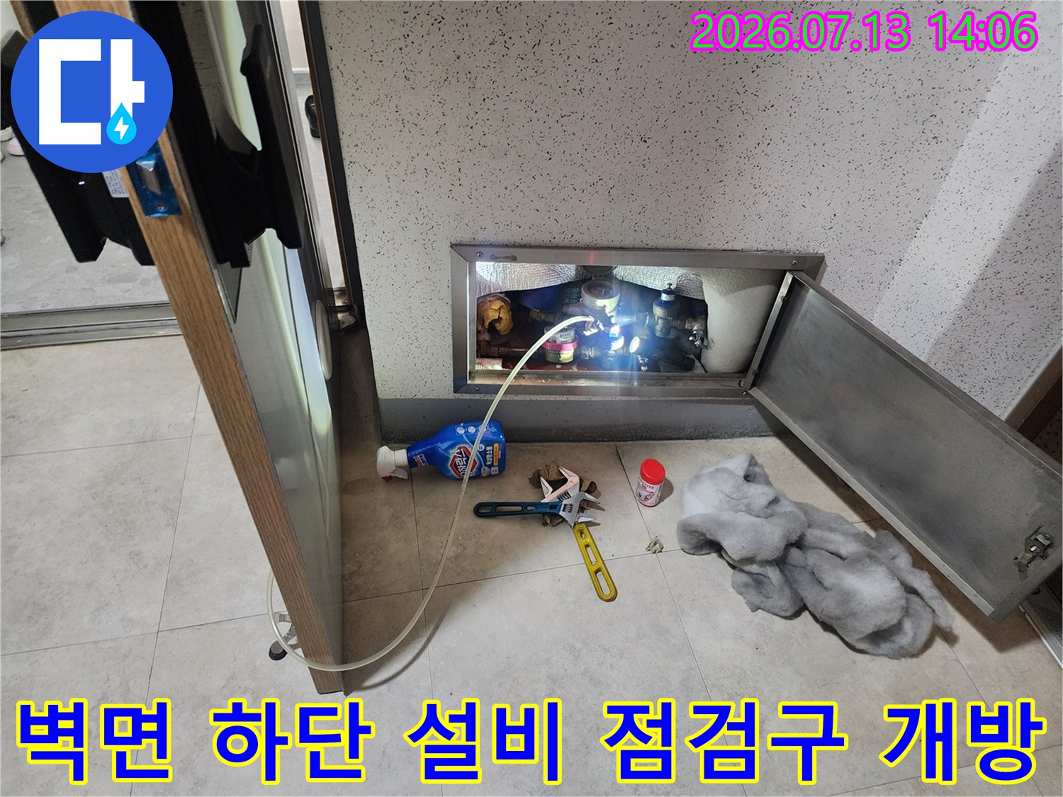 은색 금속 재질의 점검구가-열려 있고 내부 배관과 작업 도구가 보이는 모습