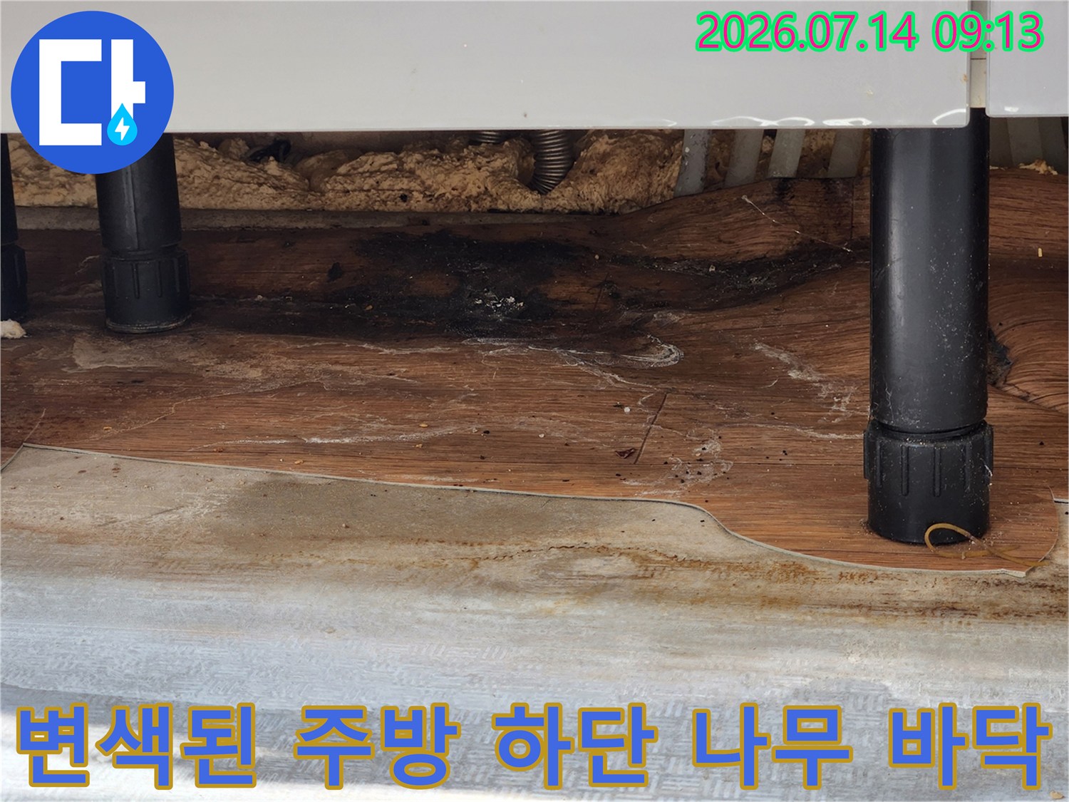 나무 바닥재가 누수로 인해 짙게 오염되어 검은 얼룩이 생긴 싱크대 하부 모습