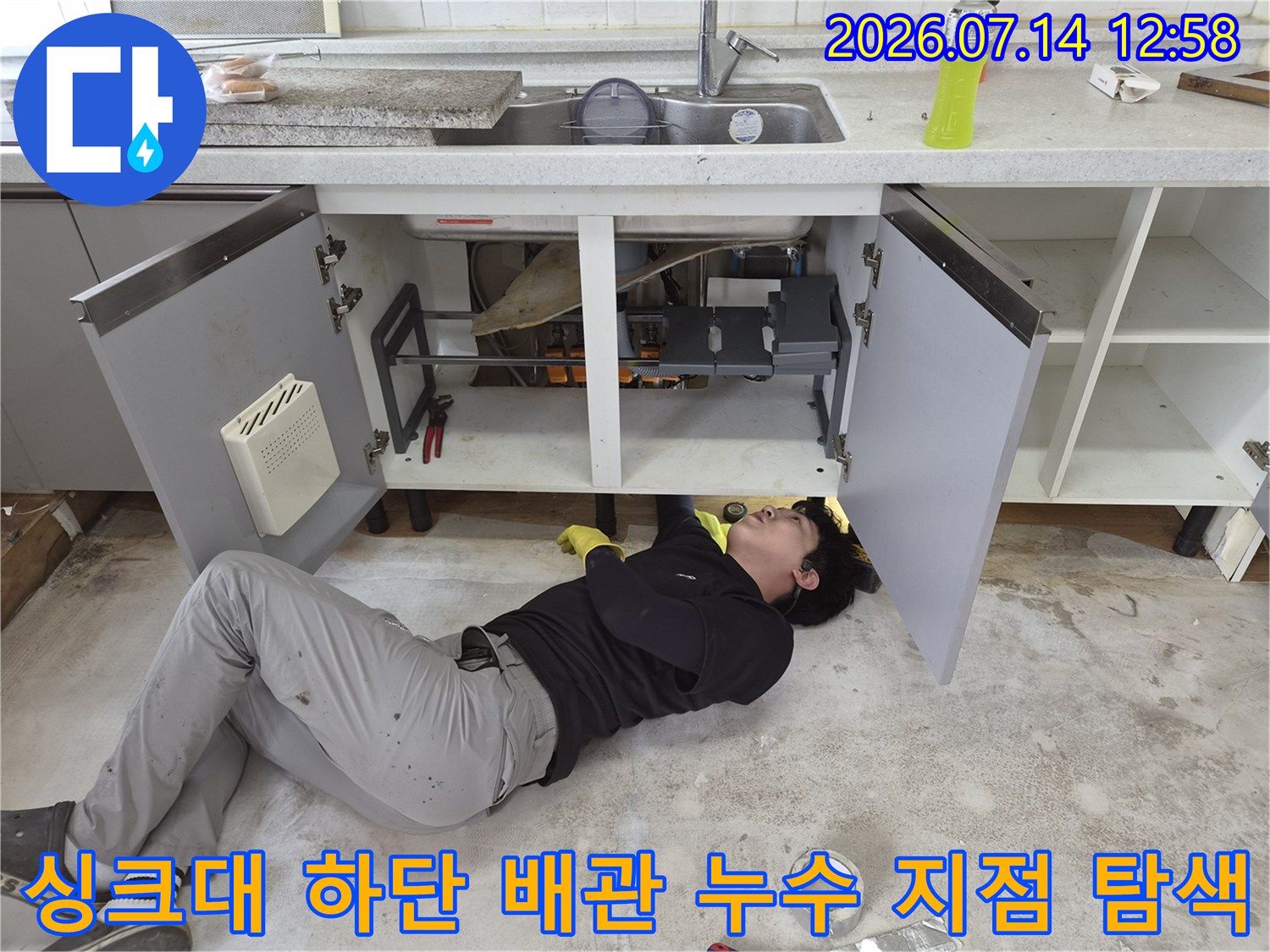 엔지니어가 싱크대 밑 좁은 공간에 몸을 넣어 배수관 상태를 관찰하는 모습