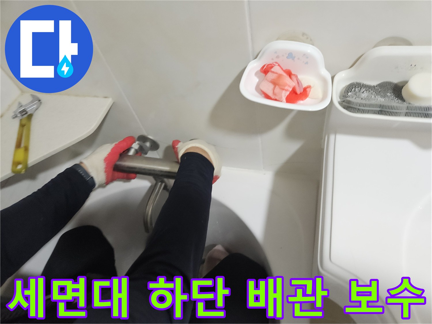 공구로 세면대 아래쪽 금속 배관 연결 지점을 조이고 있는 수리 장면