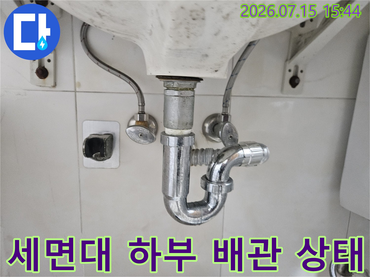 세면대 아래쪽의 트랩과 호스 연결부를 포함한 전체 배관 시스템을 점검하는 사진입니다.