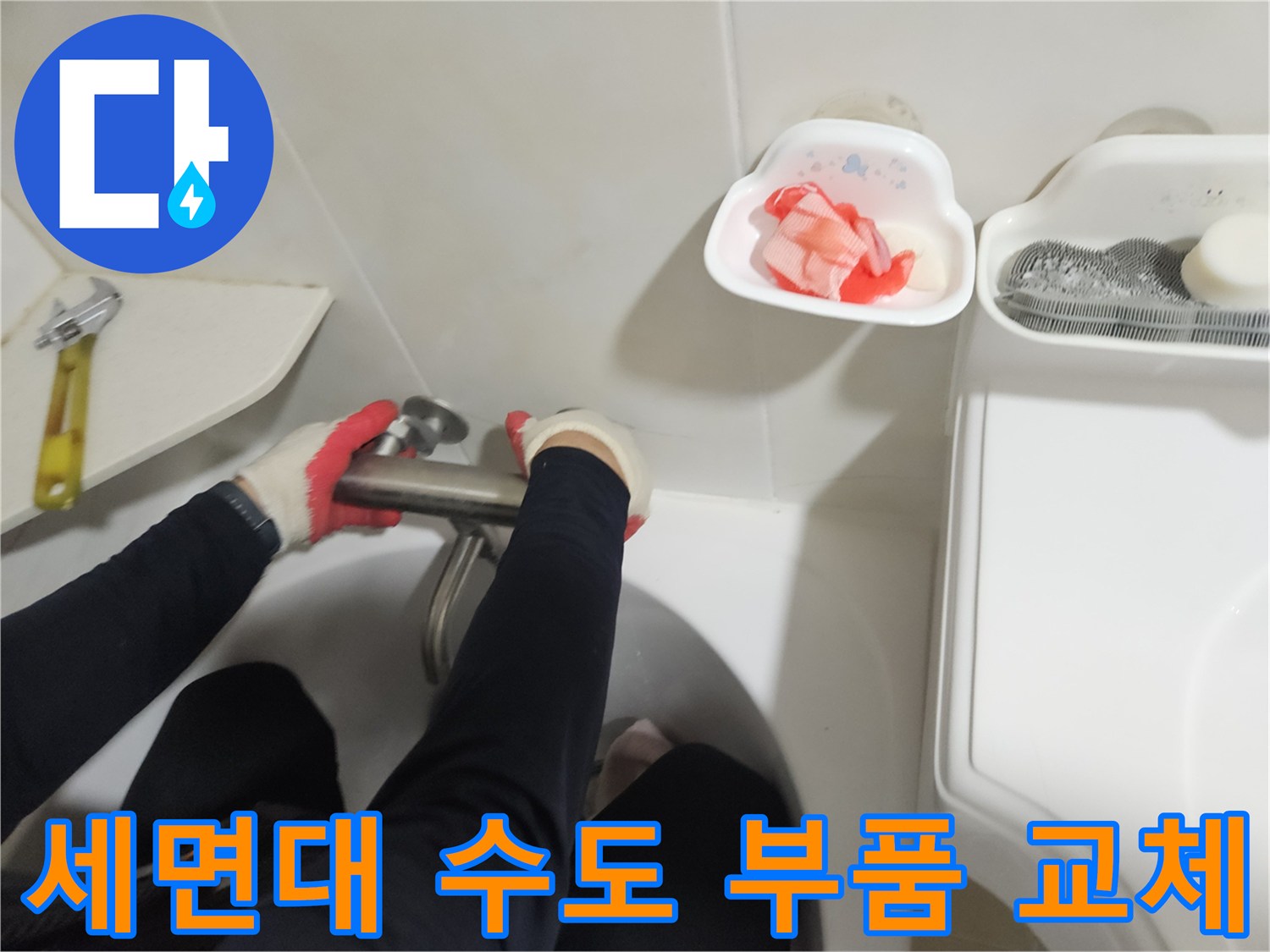 화장실 세면대 아래쪽 금속 배관을 공구로 조작하는 보수 작업 사진
