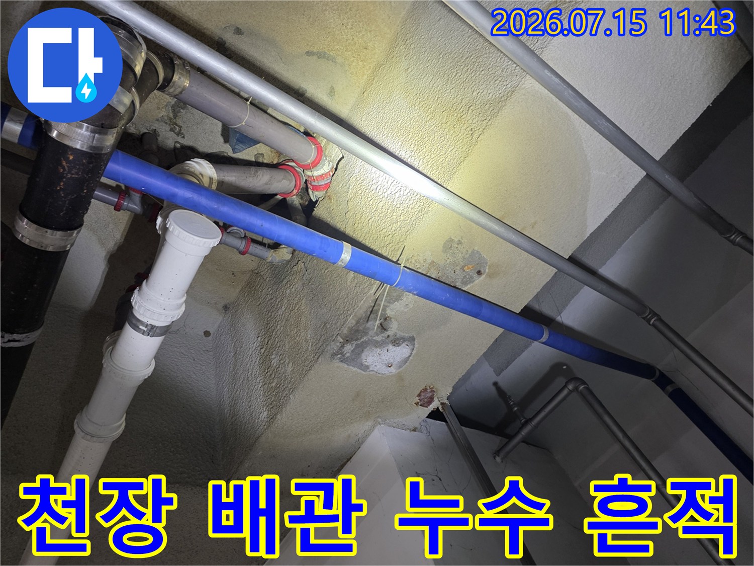 콘크리트 천장에 설치된 파란색과 흰색 배관 주변으로 노란색 물 얼룩이 퍼져 있는 모습