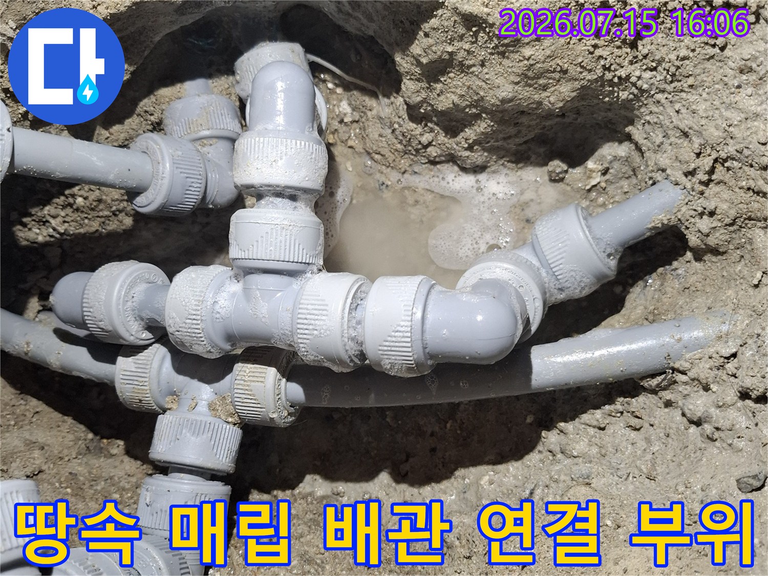 흙 속에 묻혀 있는 회색 플라스틱 수도 배관과 여러 개의 연결 조인트-부품 모습