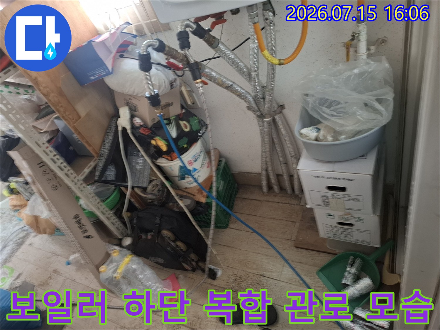 흰색 벽면에 설치된 보일러-하단의 은색 주름관과 파란색 호스가 연결된 상세 모습