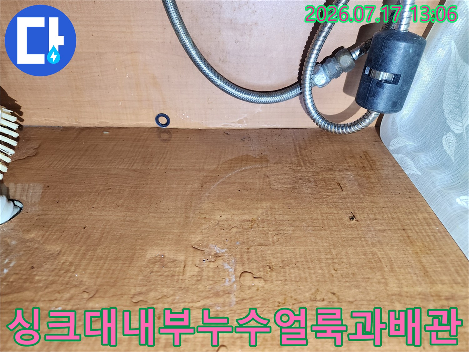 갈색으로 변한 싱크대 하부장 나무판-그 앞에 설치된 금속제 급수 배관 호스
