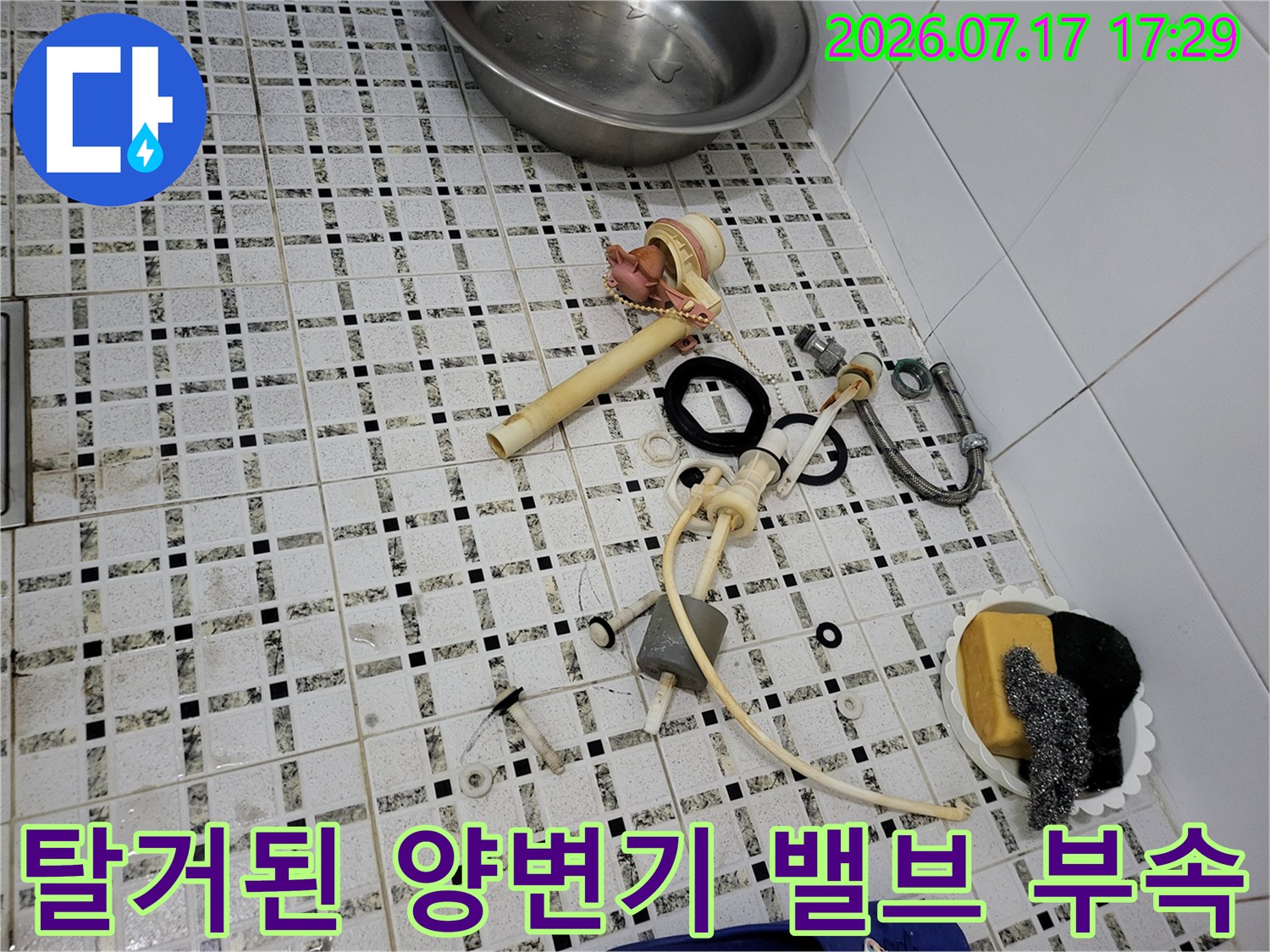 분해된-양변기 급수 호스와 필밸브 및 연결 부품들이 타일 위에 놓인 모습