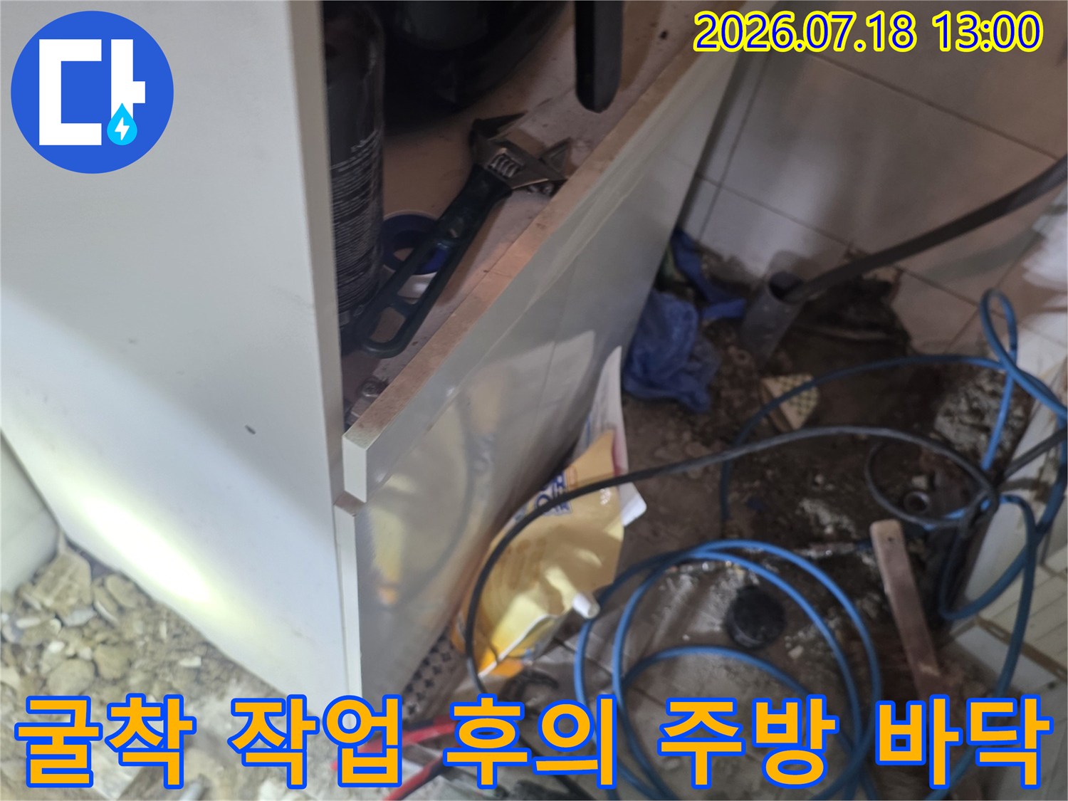 싱크대 하단부 타일을 제거하고 파란색 수도 배관과 빨간색 손잡이 펜치가 놓인 현장