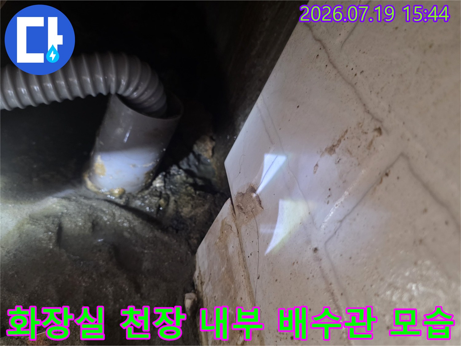 흰색 타일 벽면과-인접한 천장 하부의-회색 플라스틱 주름관-배관 연결 상태 사진