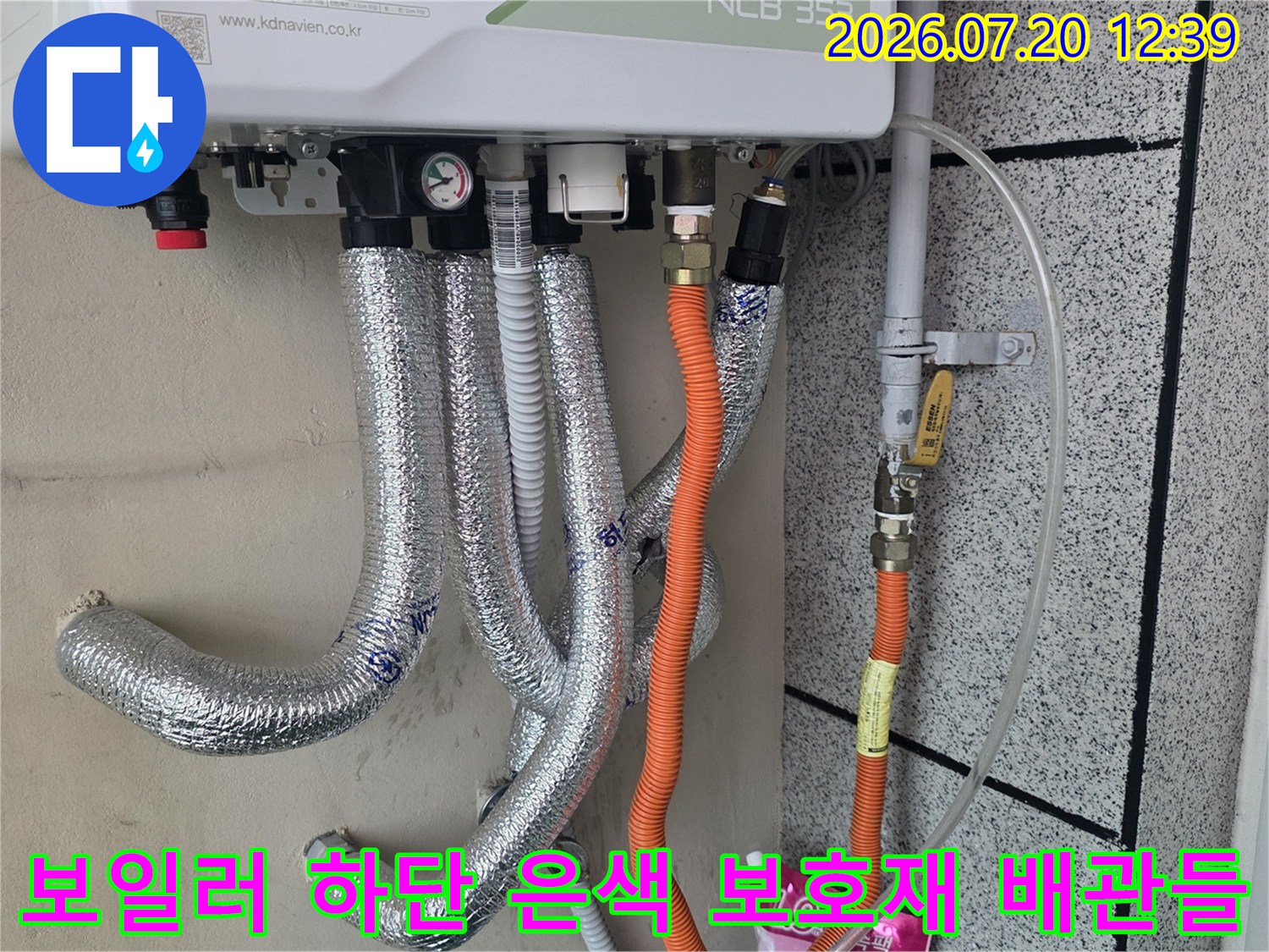 흰색 보일러 아래쪽으로 여러 갈래의 은색 단열재 배관과 주황색 관이 설치된 모습