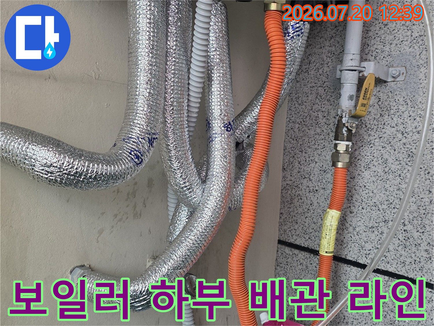 흰색 보일러 아래쪽으로 은색과 주황색 배관들이 분배기로 연결된 모습