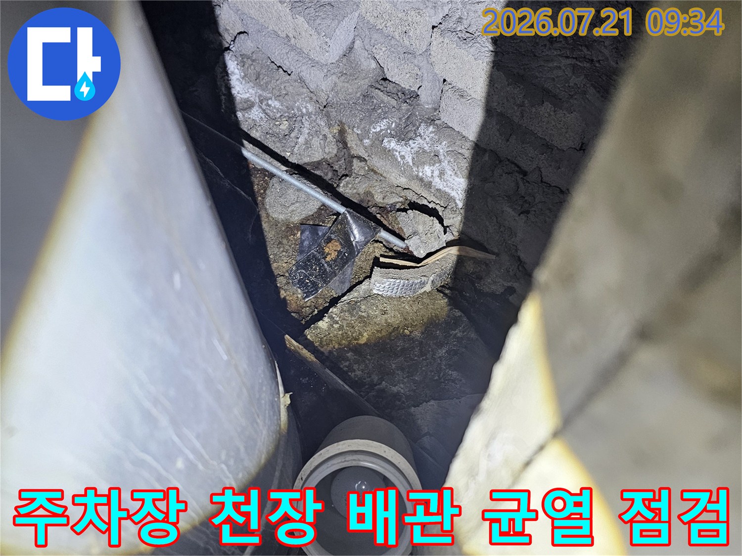 지하 주차장 천장의 노출된 배관과 콘크리트 슬래브의 균열 부위를 정밀하게 점검하는 모습