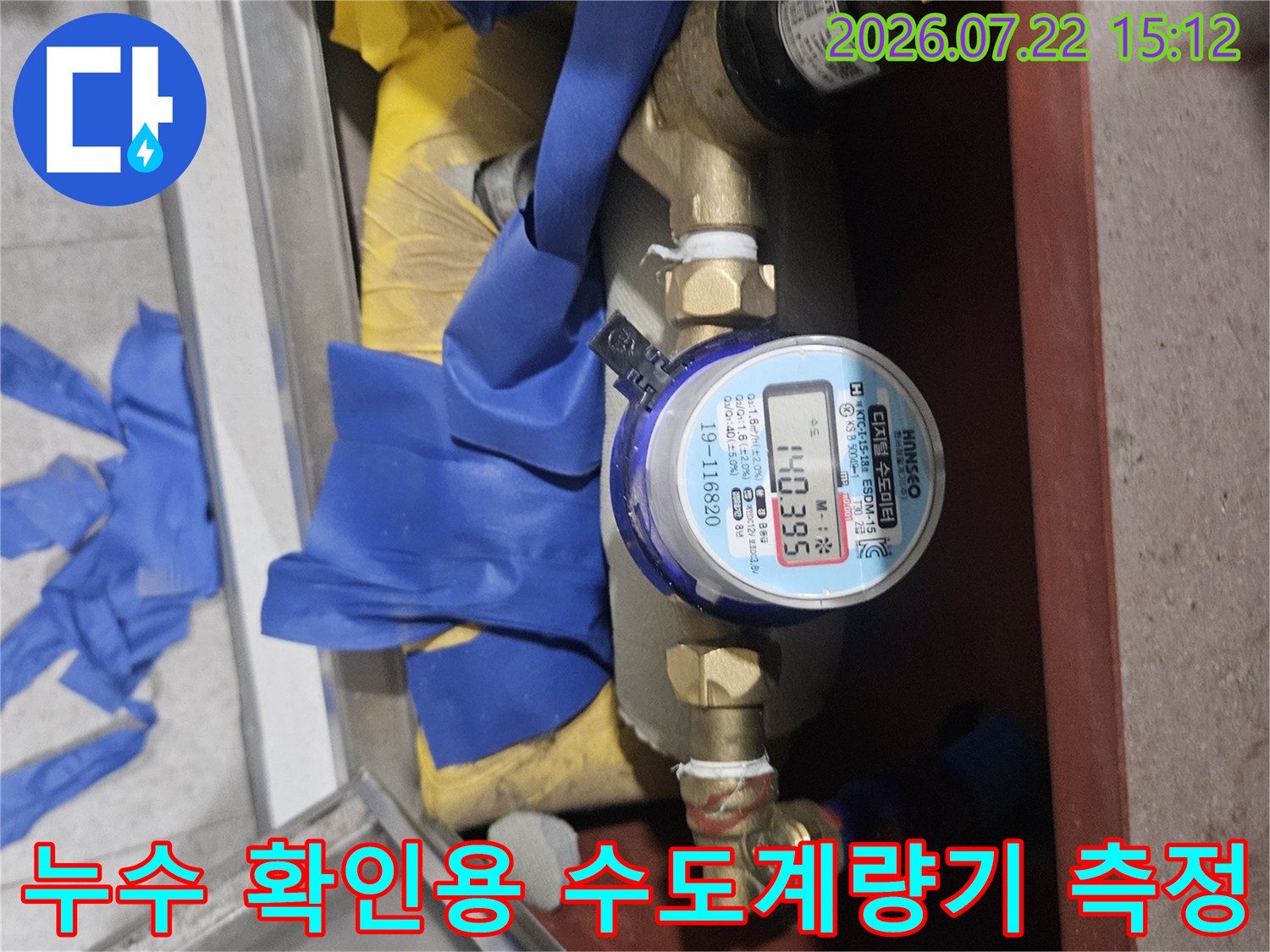 숫자가 표시된 원형 수도계량기와 주변의 파란색 보호재-금속 배관 연결부