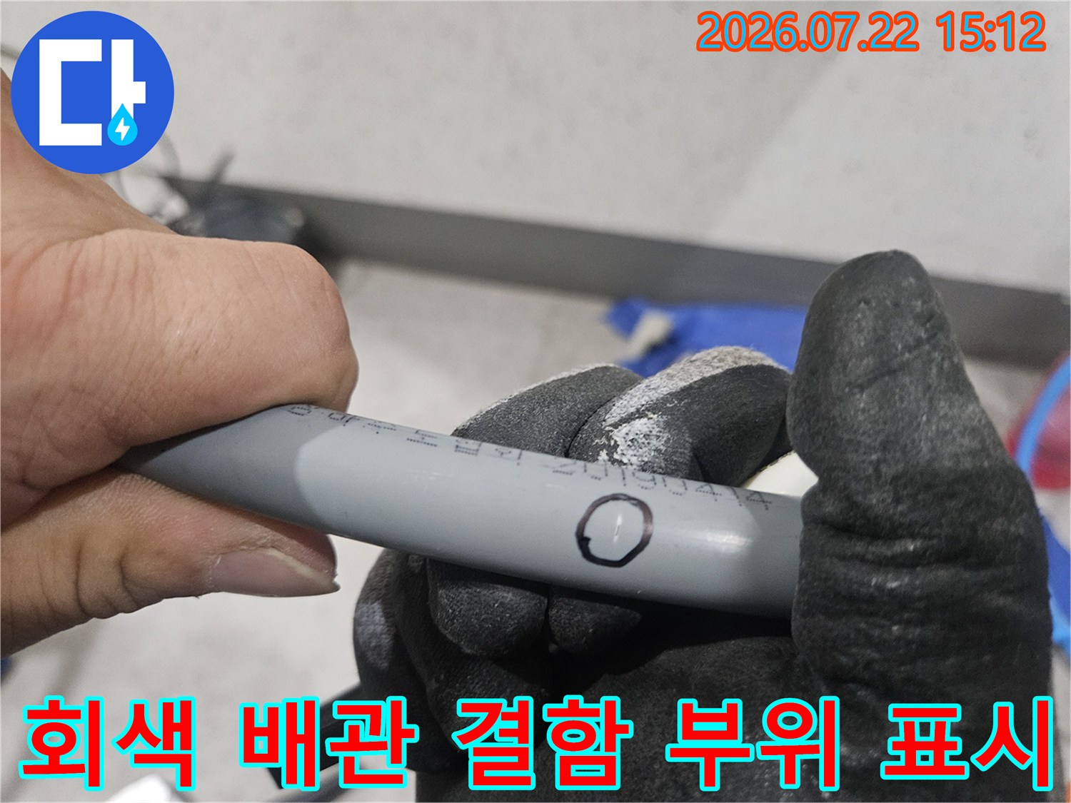 작업자가 장갑을 낀 손으로 회색 배관의 누수 지점에 표시된 원형 마킹을 가리키는 사진