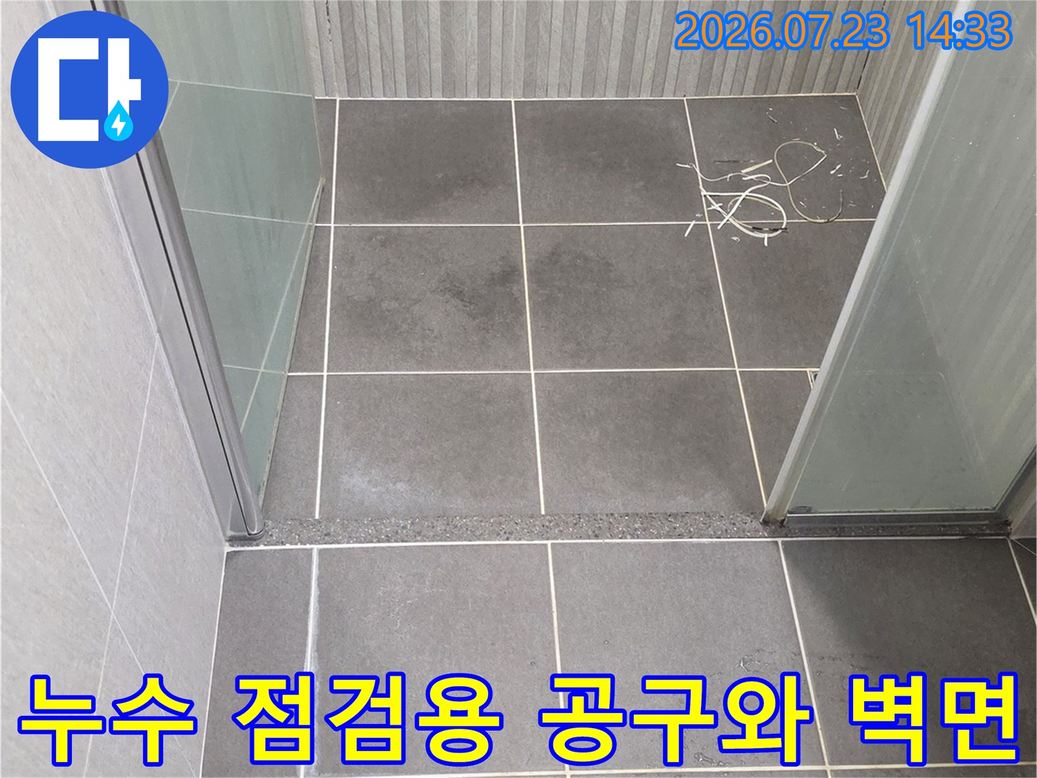욕실의 회색 타일 벽과 그 하단에 놓인 파란색 손잡이 렌치-공구 사진