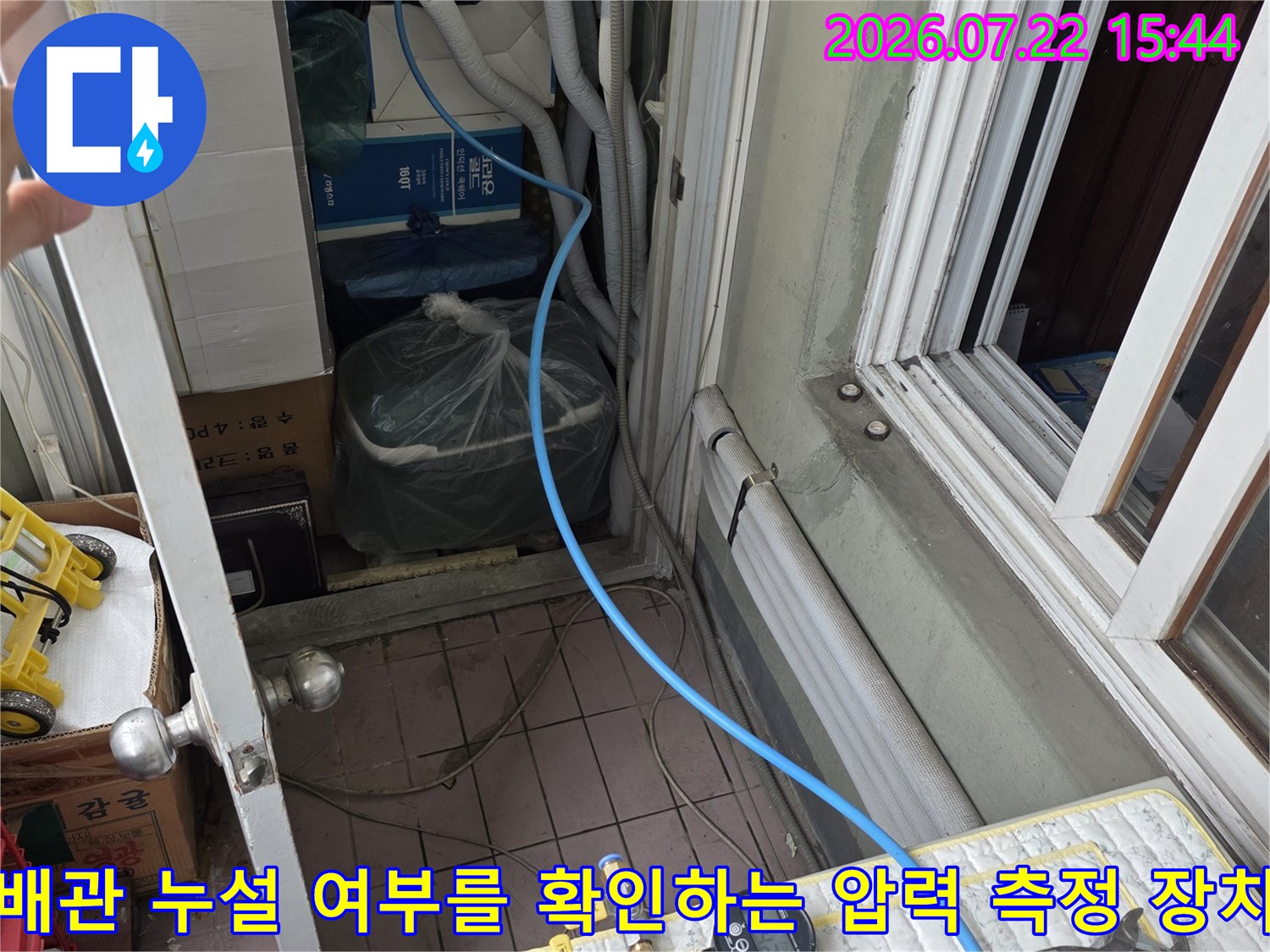 파란색 호스가 연결된 압력 게이지 세트-바닥에 놓인 공구와 배관 연결부 모습