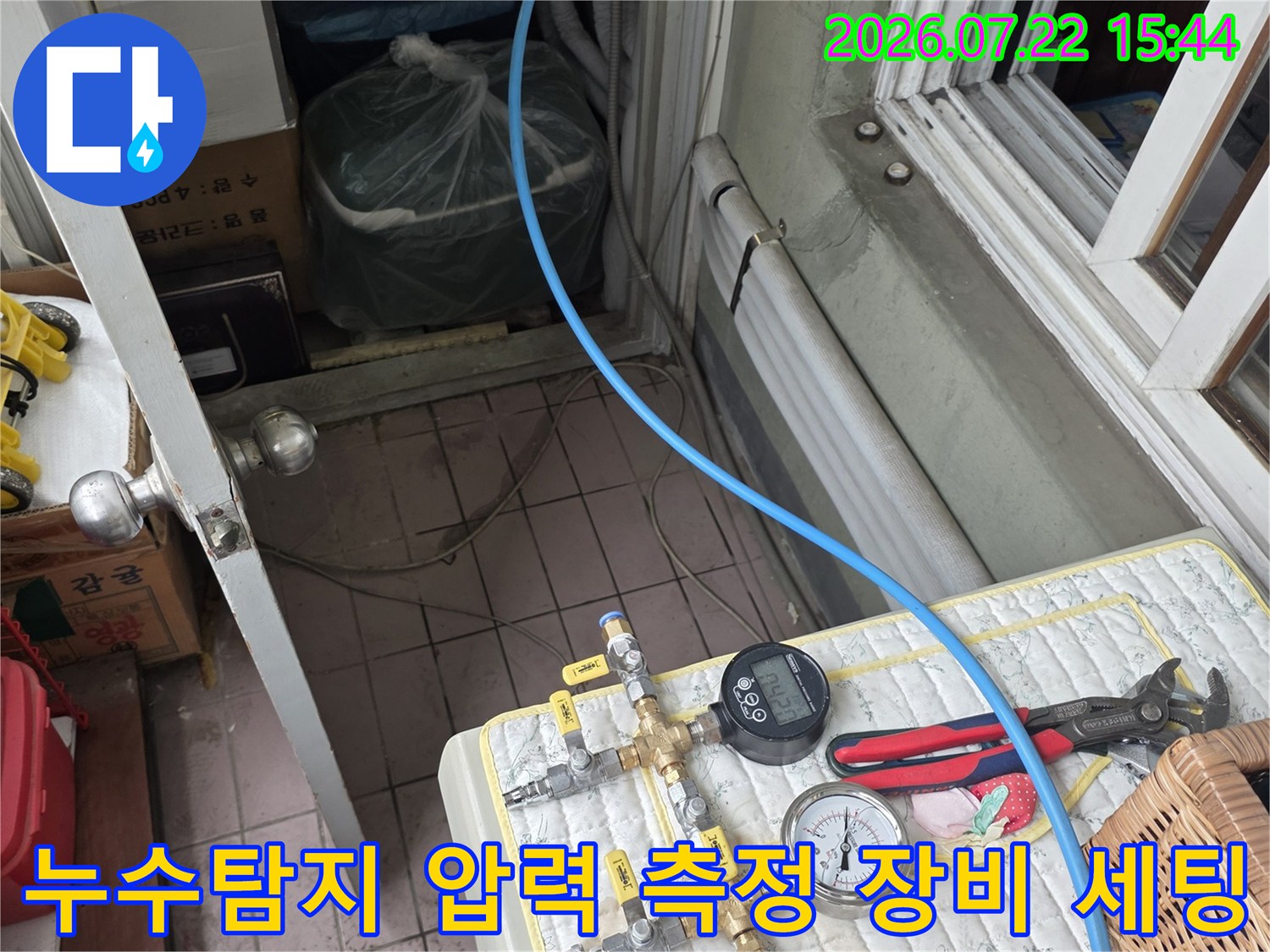 흰색 매트 위에 놓인 디지털 압력계와 아날로그 게이지-파란색 호스가 연결된 누수 탐지 장비 모습