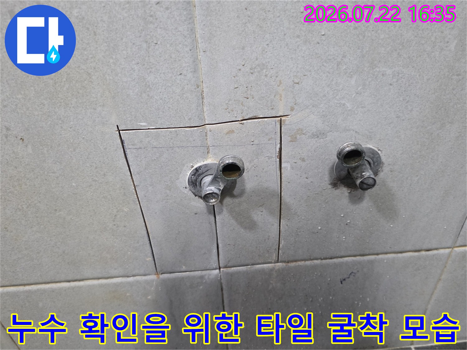 밝은 회색 타일 벽면에 직사각형 모양으로 구멍이 나 있고 내부의 금속 배관이 드러난 장면