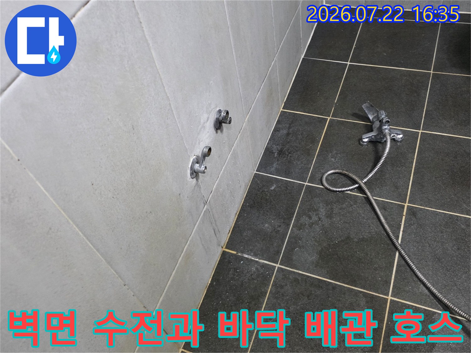 짙은 색상의 타일 벽면에 돌출된 수도꼭지와 그 아래로 길게 늘어진 샤워 호스의 모습