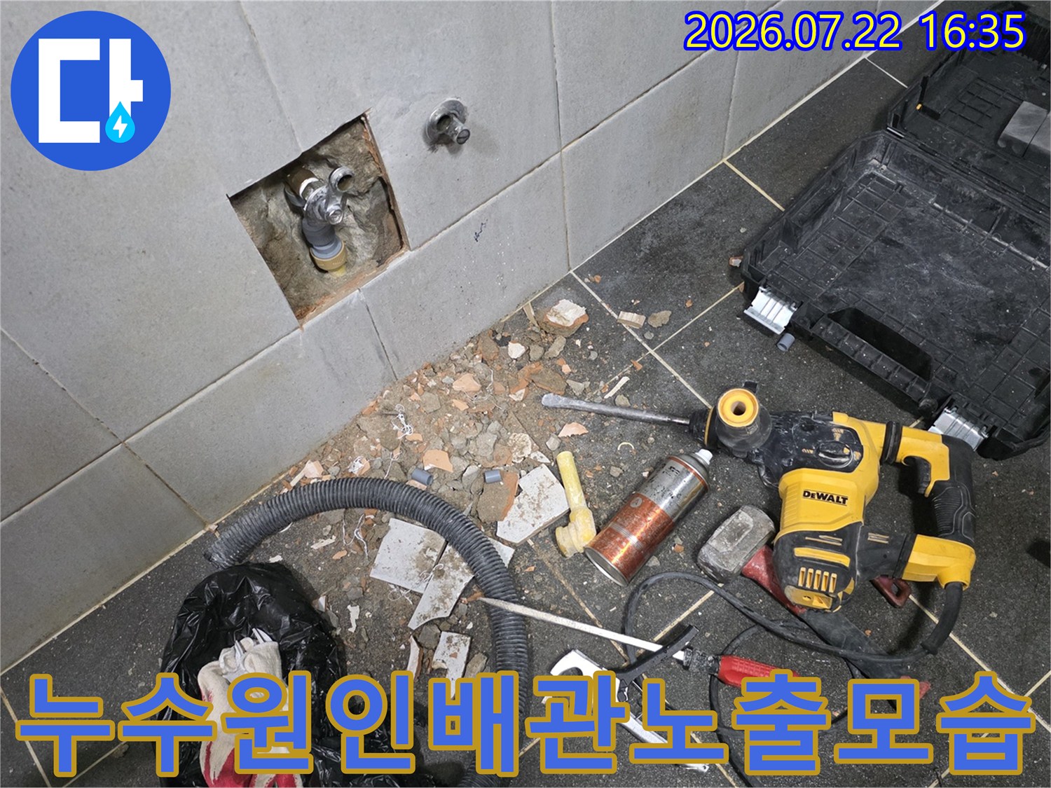 타일 벽면의 일부를 제거하여 내부 금속 배관과 부속품이 드러나 있고 바닥엔 공구들이 흩어져 있는 모습