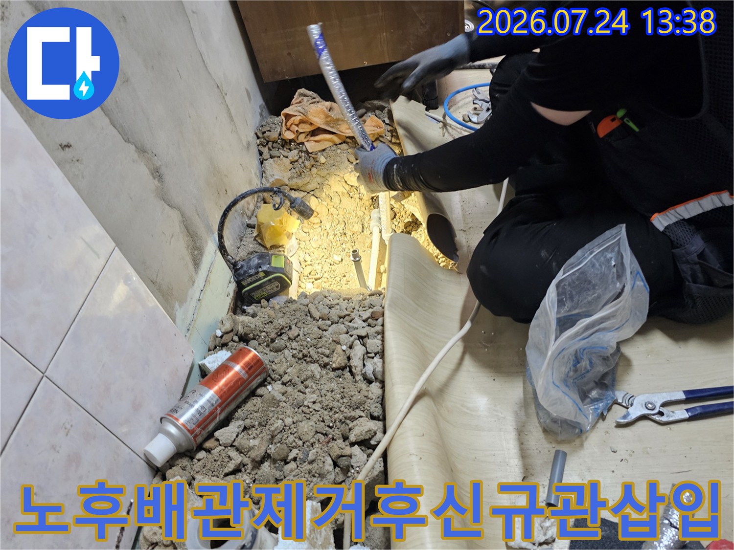 굴착된 흙 바닥 위로 파란색 보온재 배관을 설치하고 있는 작업자의 손과 장비 모습