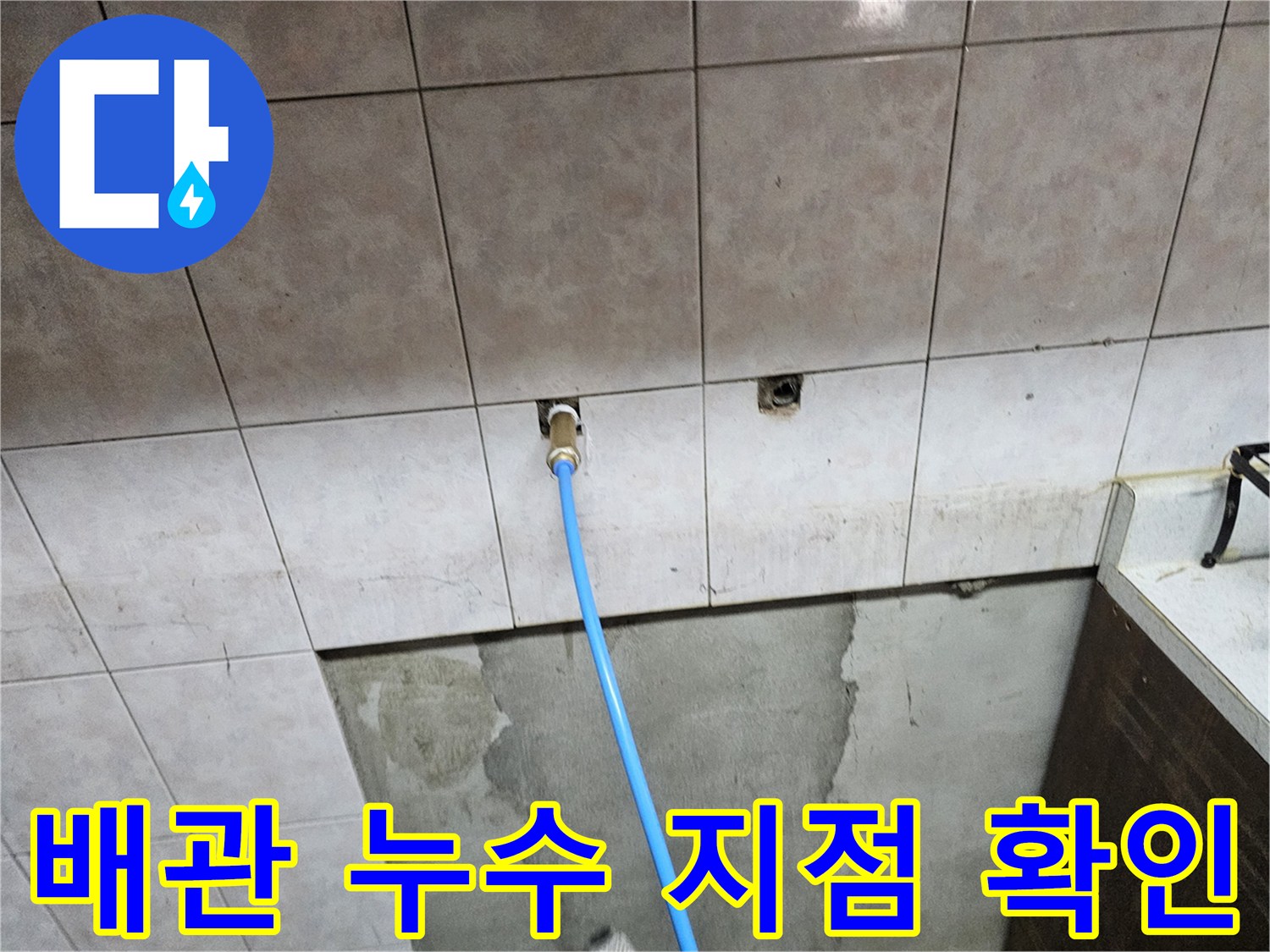 타일 벽면 배관구에 연결된 파란색 점검용 호스 상세 사진