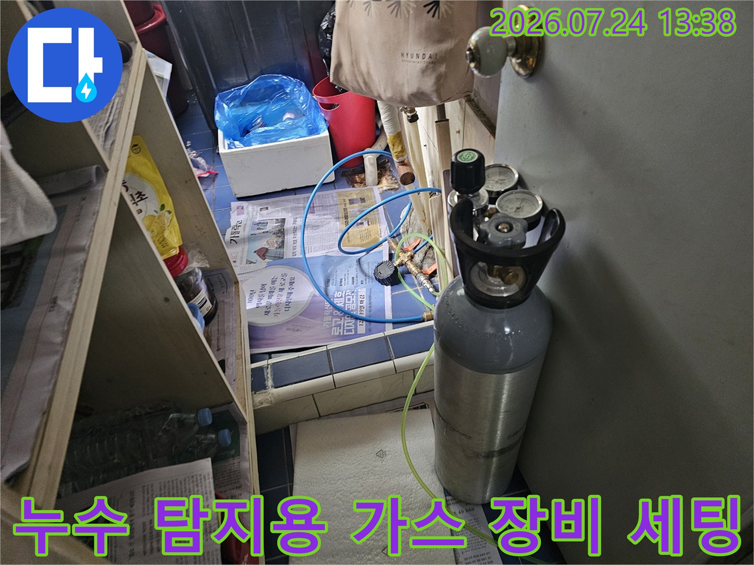회색빛 누수 탐지용 가스 실린더와 파란색 연결 호스가 바닥에 놓여 있는 모습
