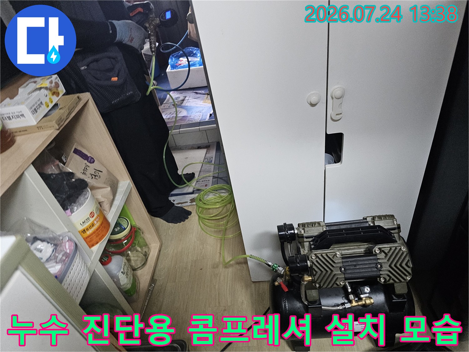 흰색 가구 옆 바닥에 배치된 누수 탐지 장비와 연결된 초록색 호스의 모습