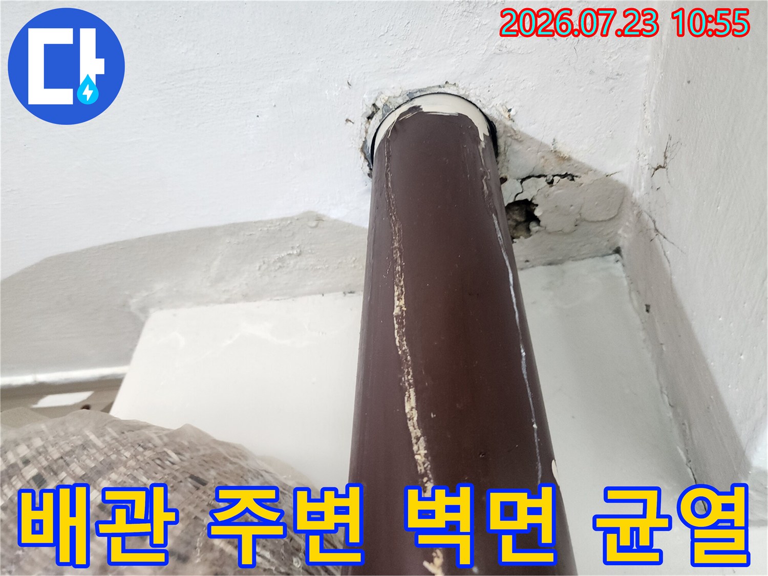 갈색 배관이 벽을 통과하는 부위에 생긴 틈새와 하얀 마감재의 파손 모습