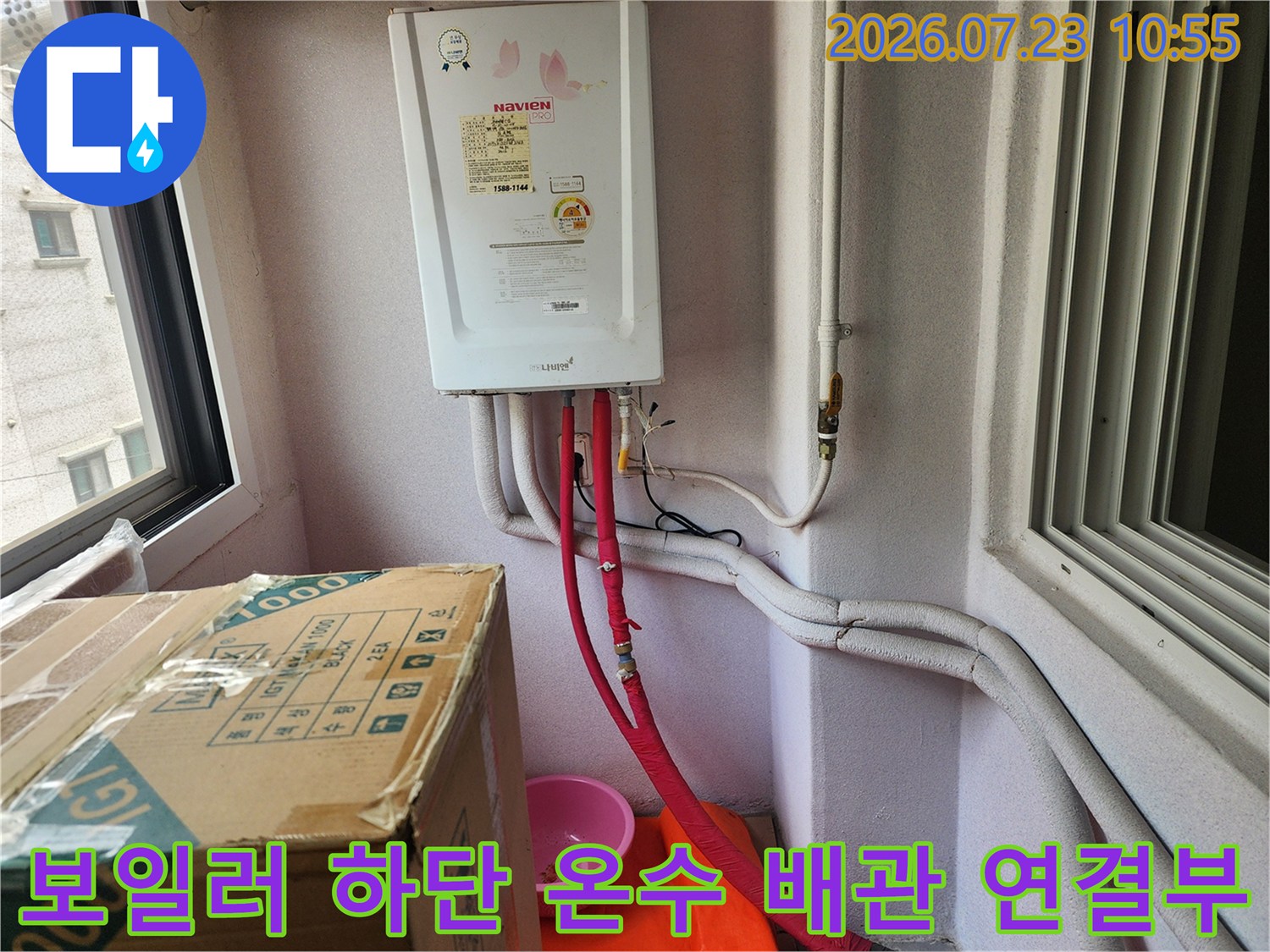 흰색 벽면에 설치된 가스 보일러와 그 아래로 연결된 붉은색 온수 배관 모습