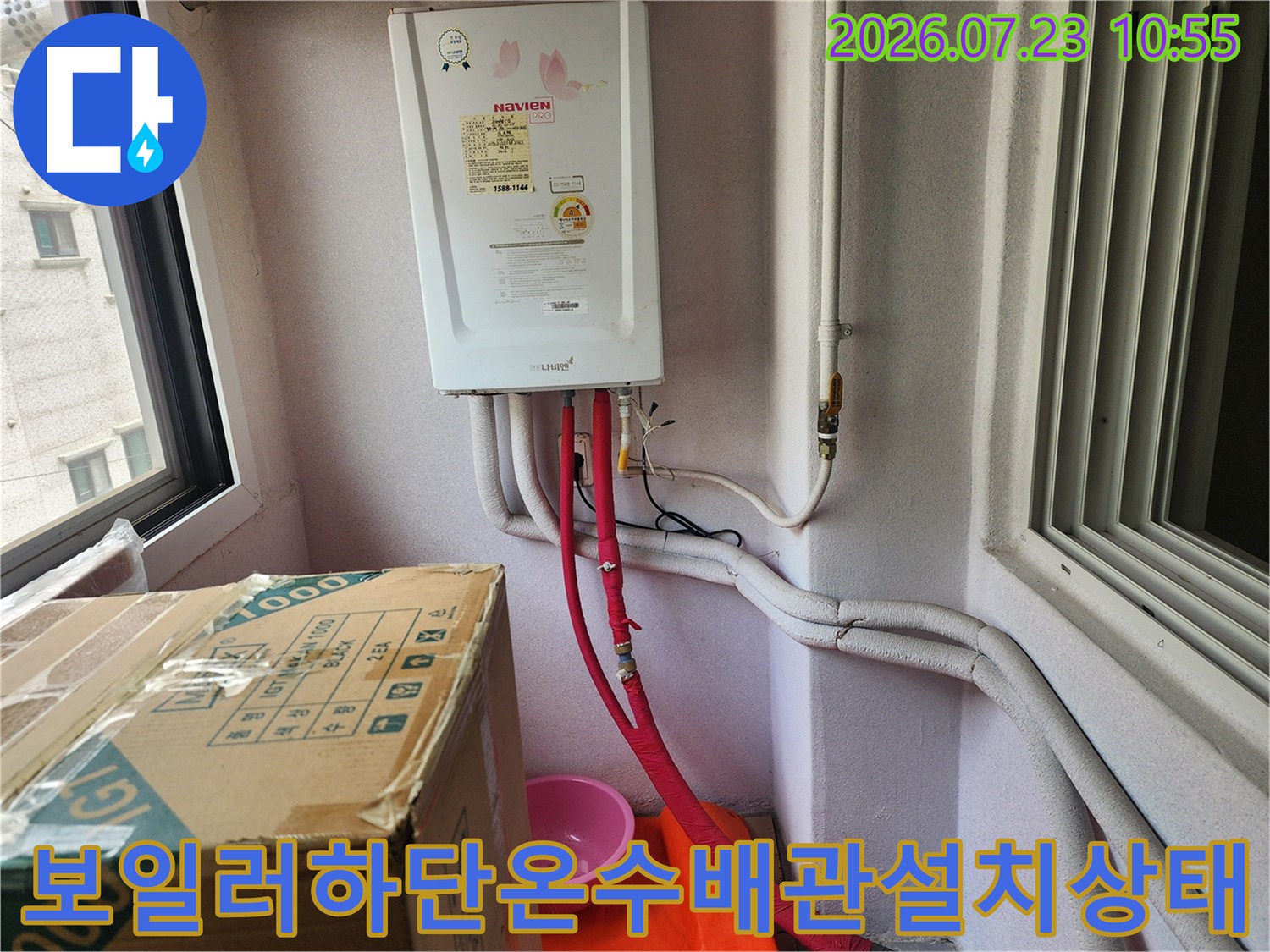 흰색 벽면에 설치된 가스보일러 하단으로 붉은색 온수 배관과 흰색 보온재 배관들이 연결되어 있는 모습