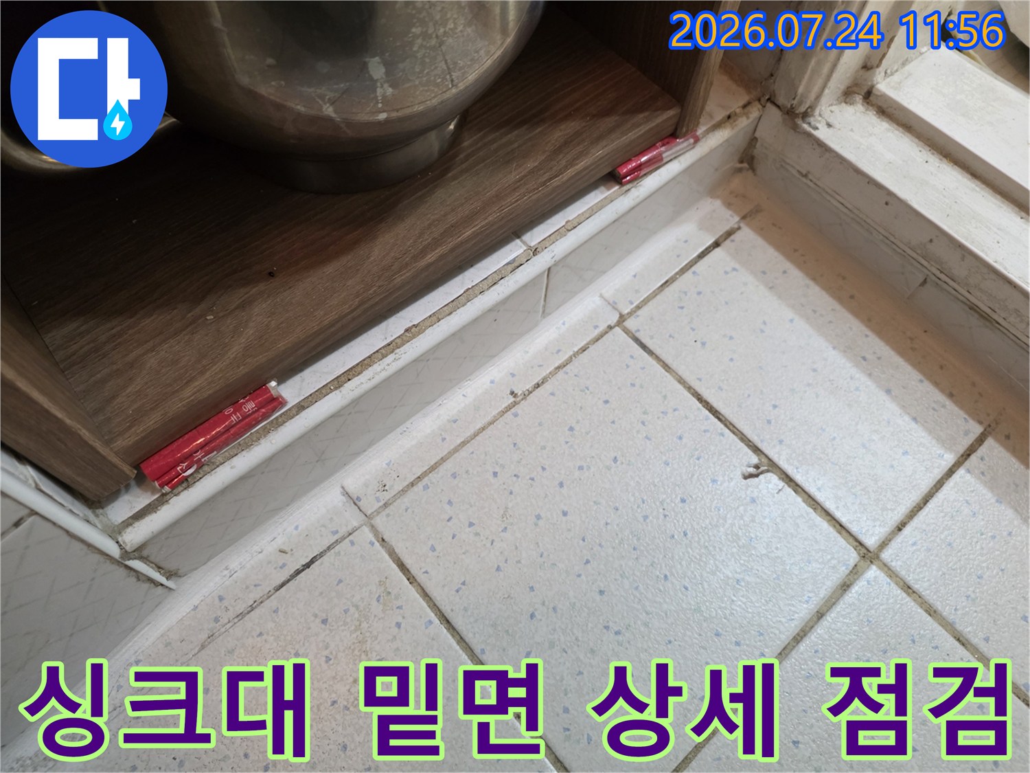 싱크대 하부를 들춰내고 바닥 타일과 배수구 연결 부위를 정밀하게 진단하는 장면입니다.