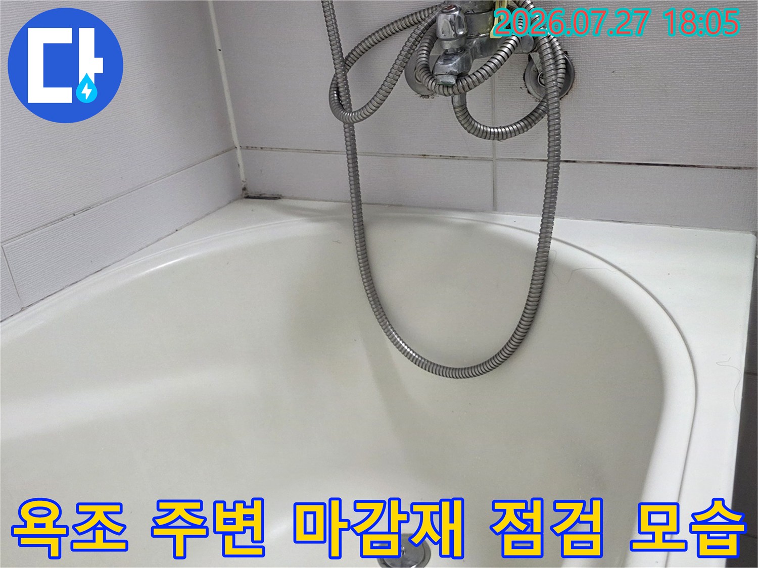 흰색 타일 벽면과 연결된 욕조의 상단부-금속 재질의 샤워 호스가 걸쳐짐