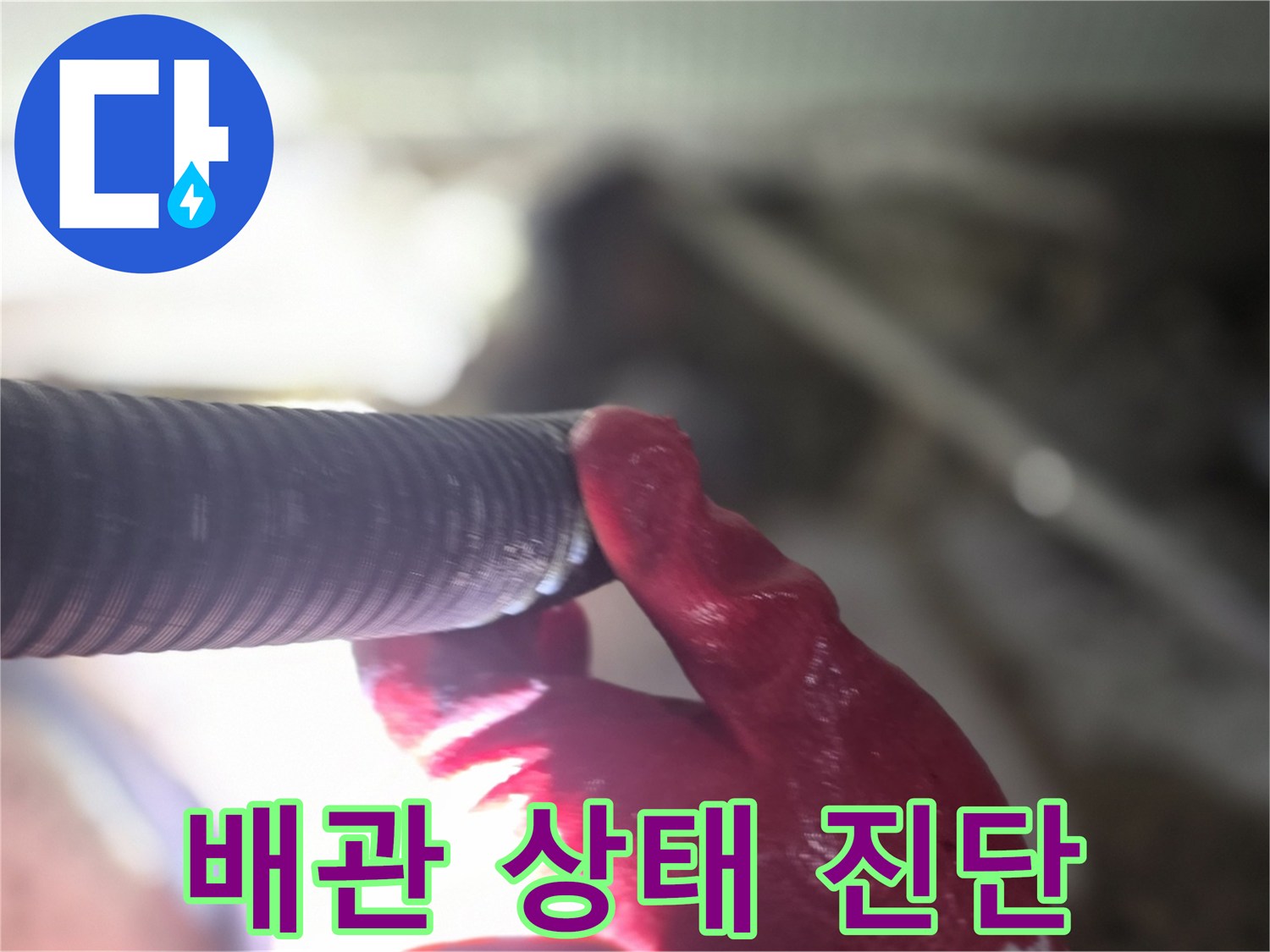 붉은색 장갑을 낀 손이 검은색 주름관 배관의 연결 부위를 살피고 있습니다.