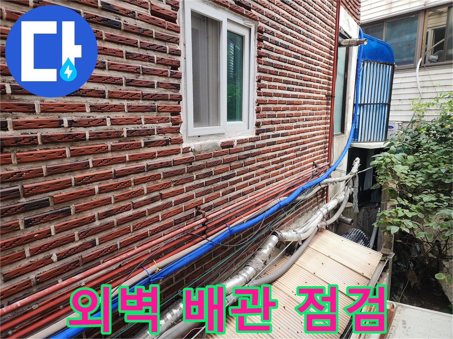 붉은 벽돌 외벽에 설치된 파란색과 은색 배관들-노출 배관 상태 확인