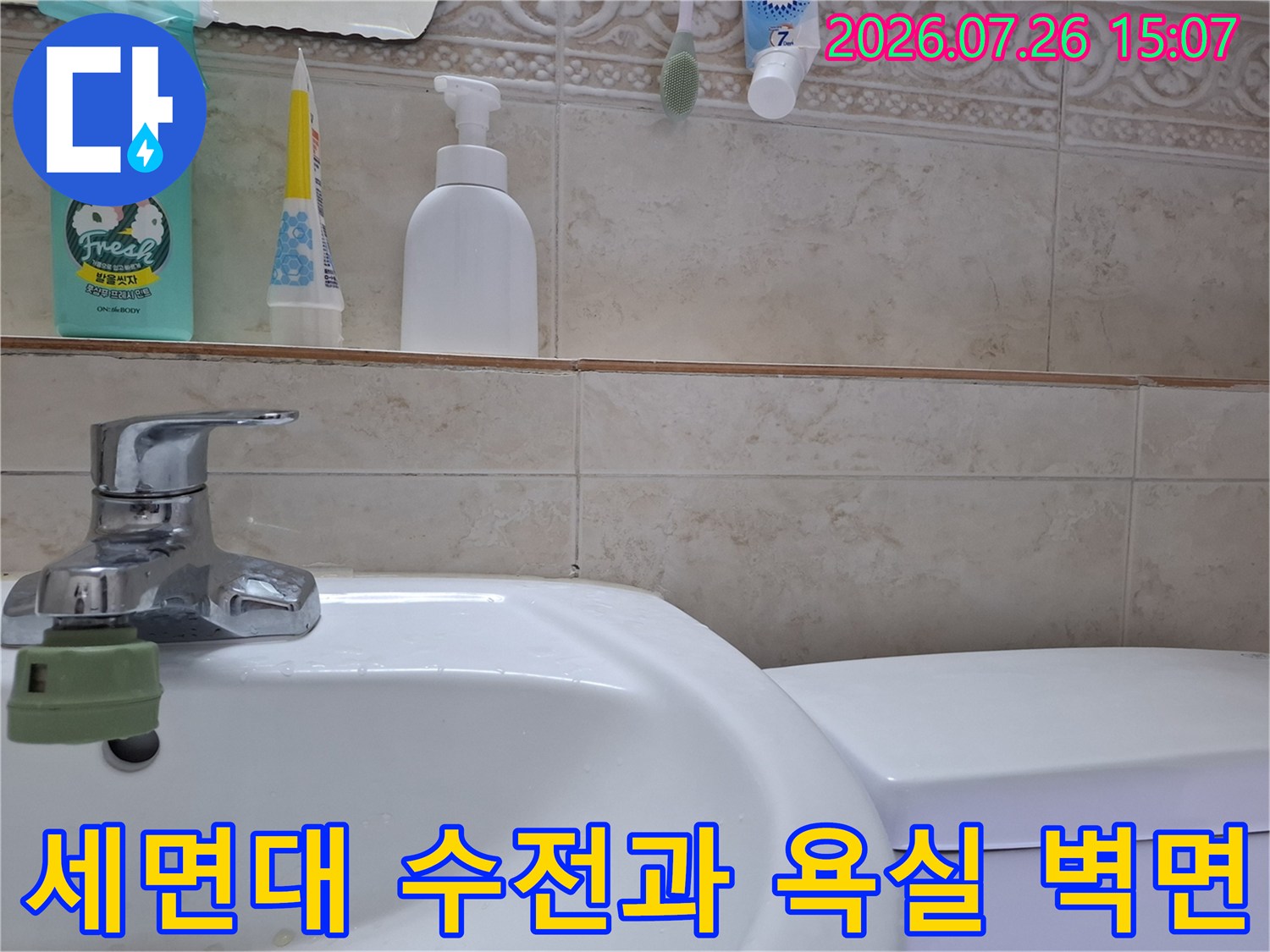 욕실 세면대 위에 놓인 세정제들과 수도꼭지-벽면 타일이 함께 찍힌 사진