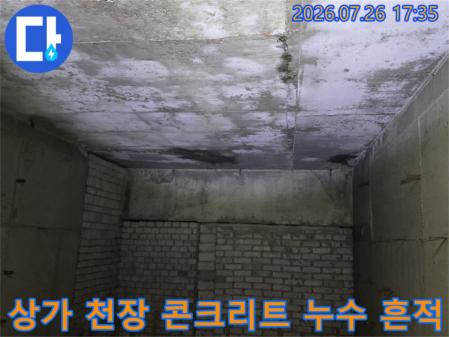 상가 건물의 노출된 콘크리트 천장에서 발생한 누수로 인해 표면이 젖어 있고 얼룩진 모습