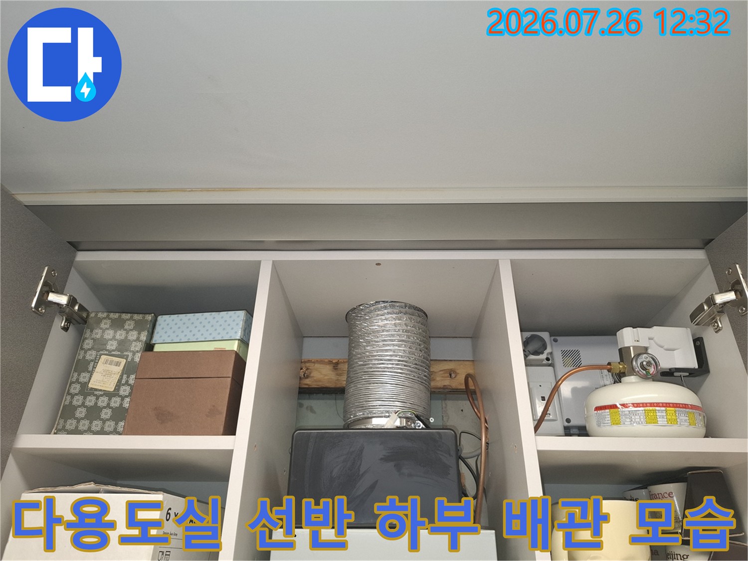 흰색 선반 아래로 은색 주름관이 내려와 있고 오른쪽에 보일러 장치가 있는- 내부 전경