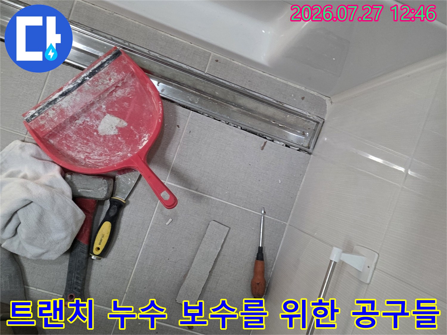 욕실 바닥-길쭉한 형태의 트랜치 배수구와 그 옆에 놓인 빨간색 헤라 및 수공구 세트