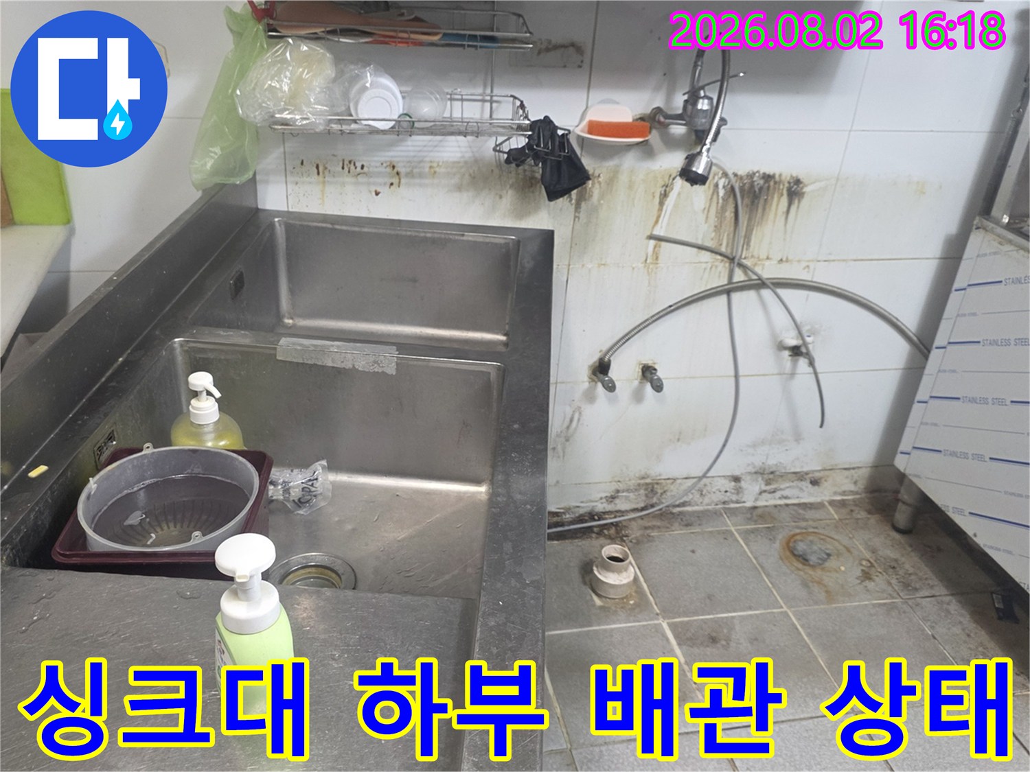 싱크대 아래 노출된 수도 배관과 벽면 타일의 누수 오염 부위
