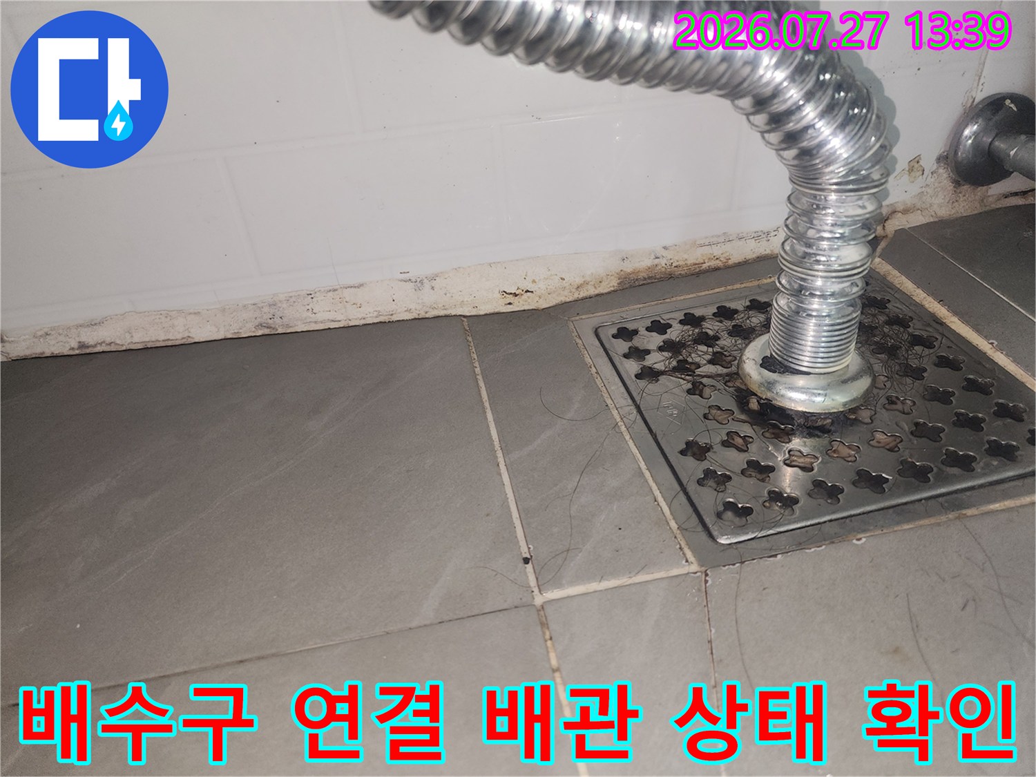 회색 타일 바닥의 스테인리스 배수구 덮개와 연결된 주름관-배관 모습