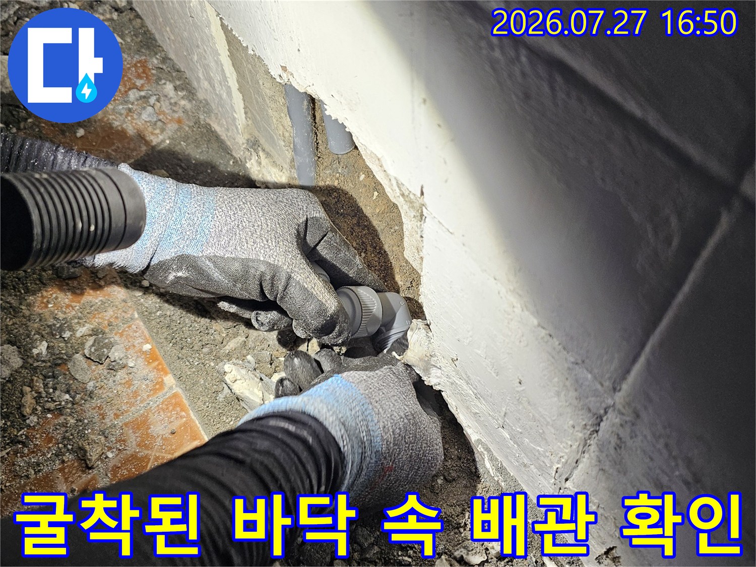 화장실 타일을 걷어내고 드러난 회색 플라스틱 배관 연결 부위를 작업자가 손으로 점검하는 모습