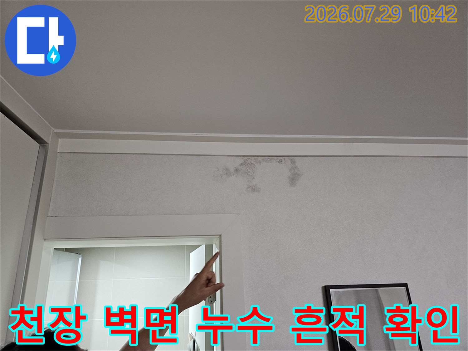 벽과 천장 경계부의 누수 자국을 손가락으로 가리키며 설명하는 장면