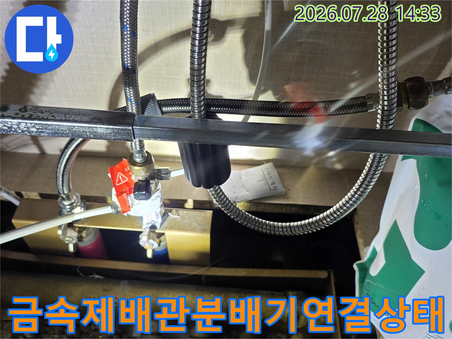 은색 스테인리스 주름관들이 황동 분배기에 연결되어 있고 붉은색 조절 밸브가 보이는 사진