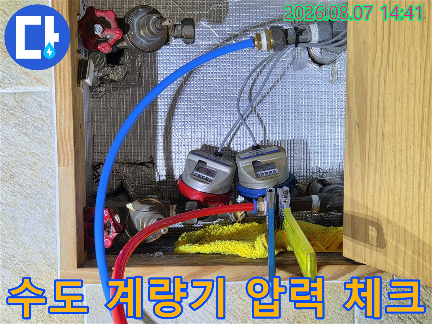 수도 계량기에 파란색과 빨<0xA5>색 호스를 연결하여 배관을 점검하는 모습입니다.