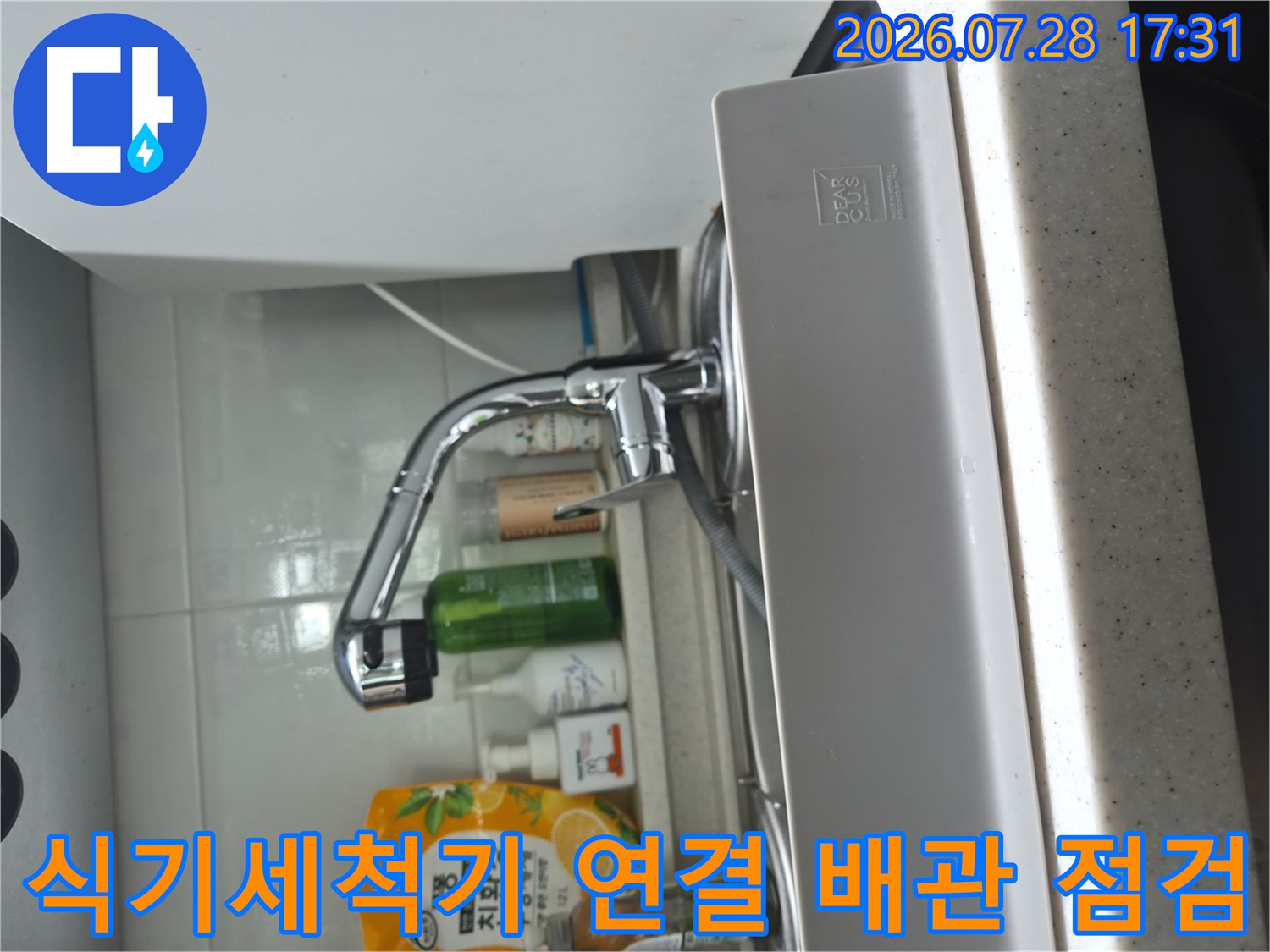 싱크대 하단에서 식기세척기를 위한 분기 밸브와 호스 연결부를 세밀하게 확인하는 사진