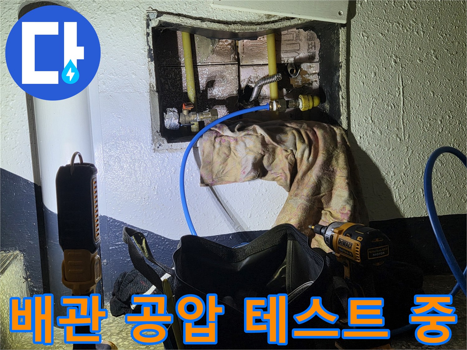 벽 내부 배관 연결 부위에 파란색 호스를 연결하여 압력을 주입하는 모습입니다.