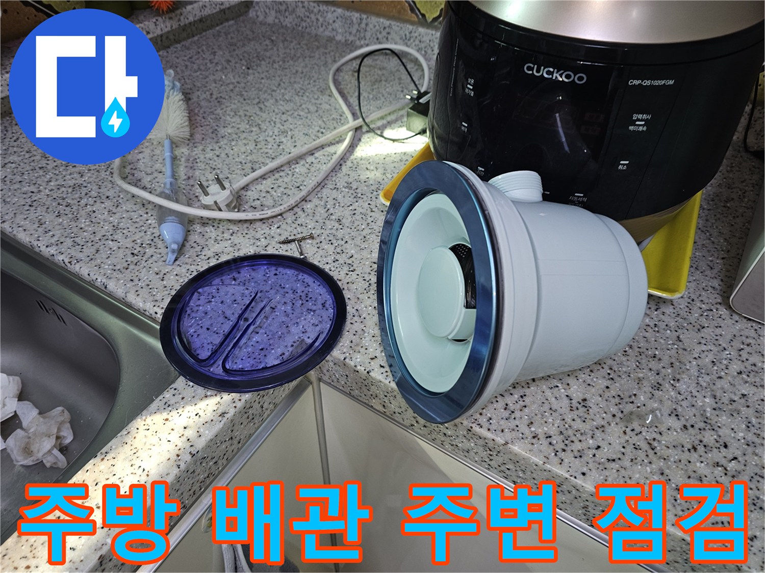 싱크대 하부의 배관 덮개와 주변 물건들이 배치된 현장 사진입니다.